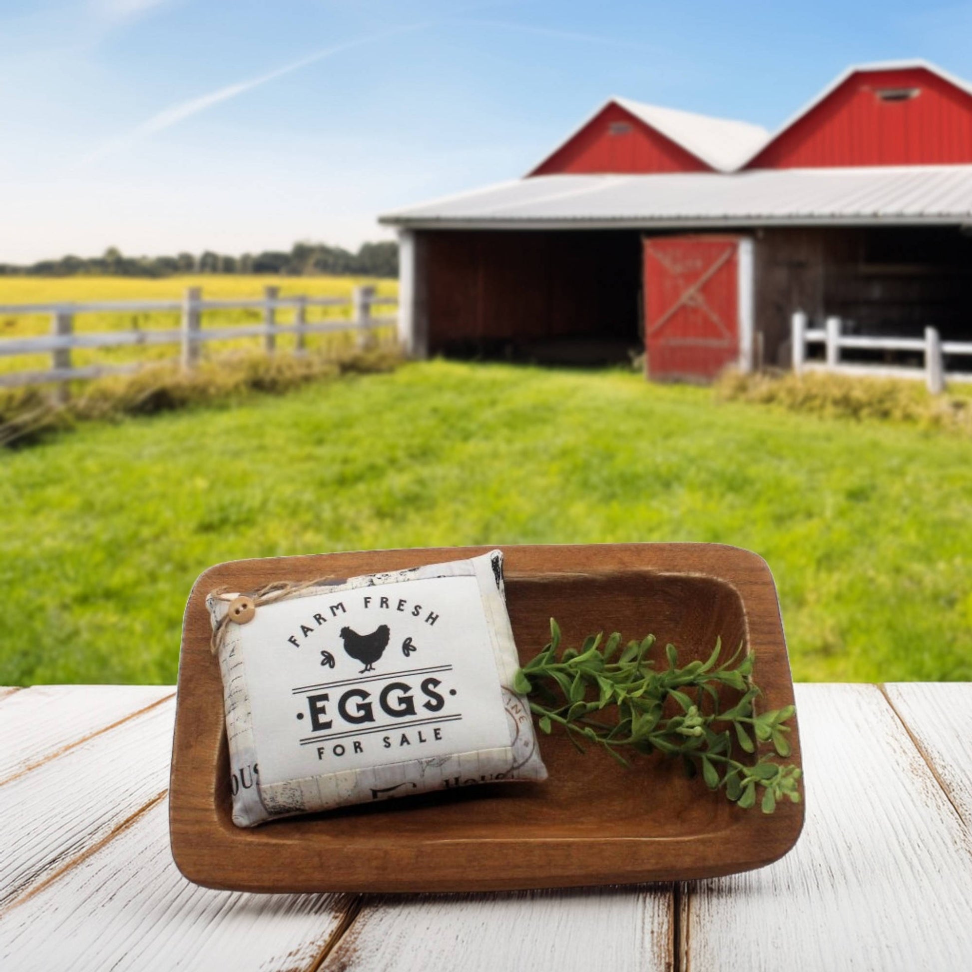 Farm fresh eggs for sale sign in a wooden basket with a barn and field in the background