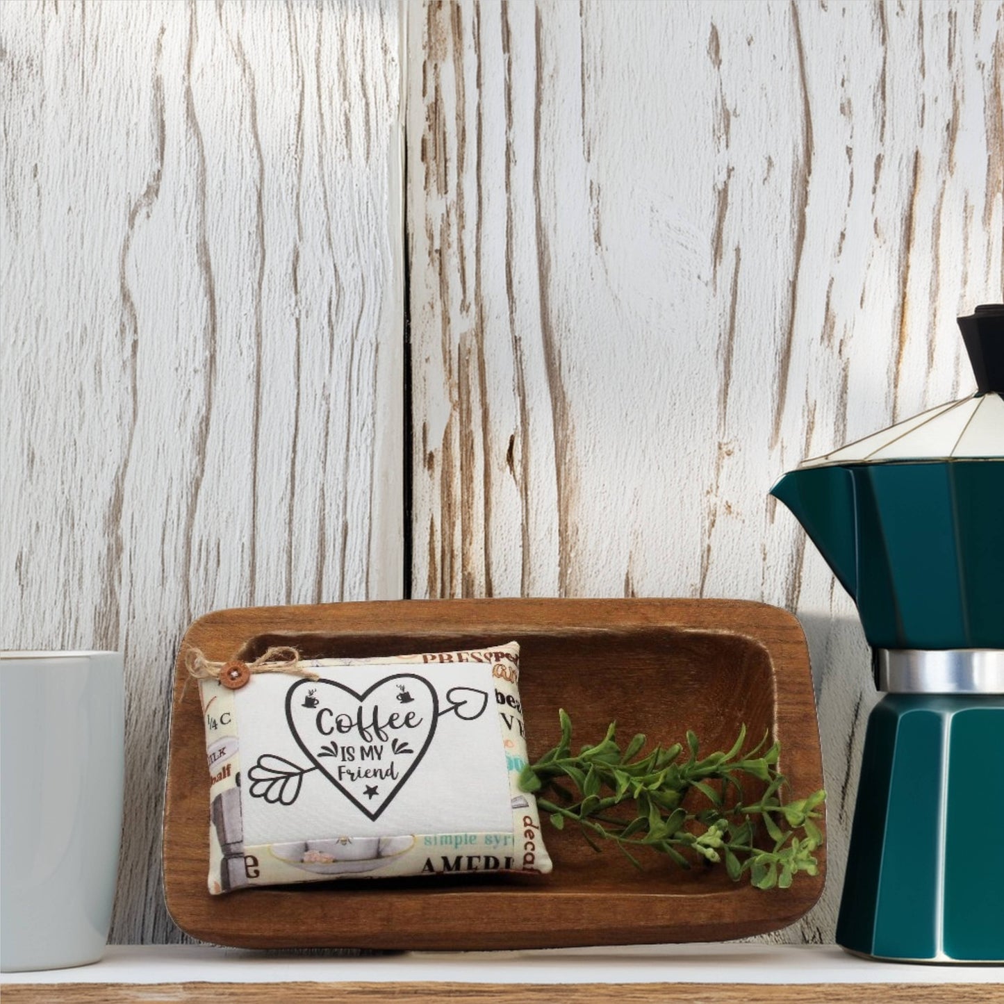 Wooden tray with a decorative item and plant on a wooden surface with a coffee maker in the background.
