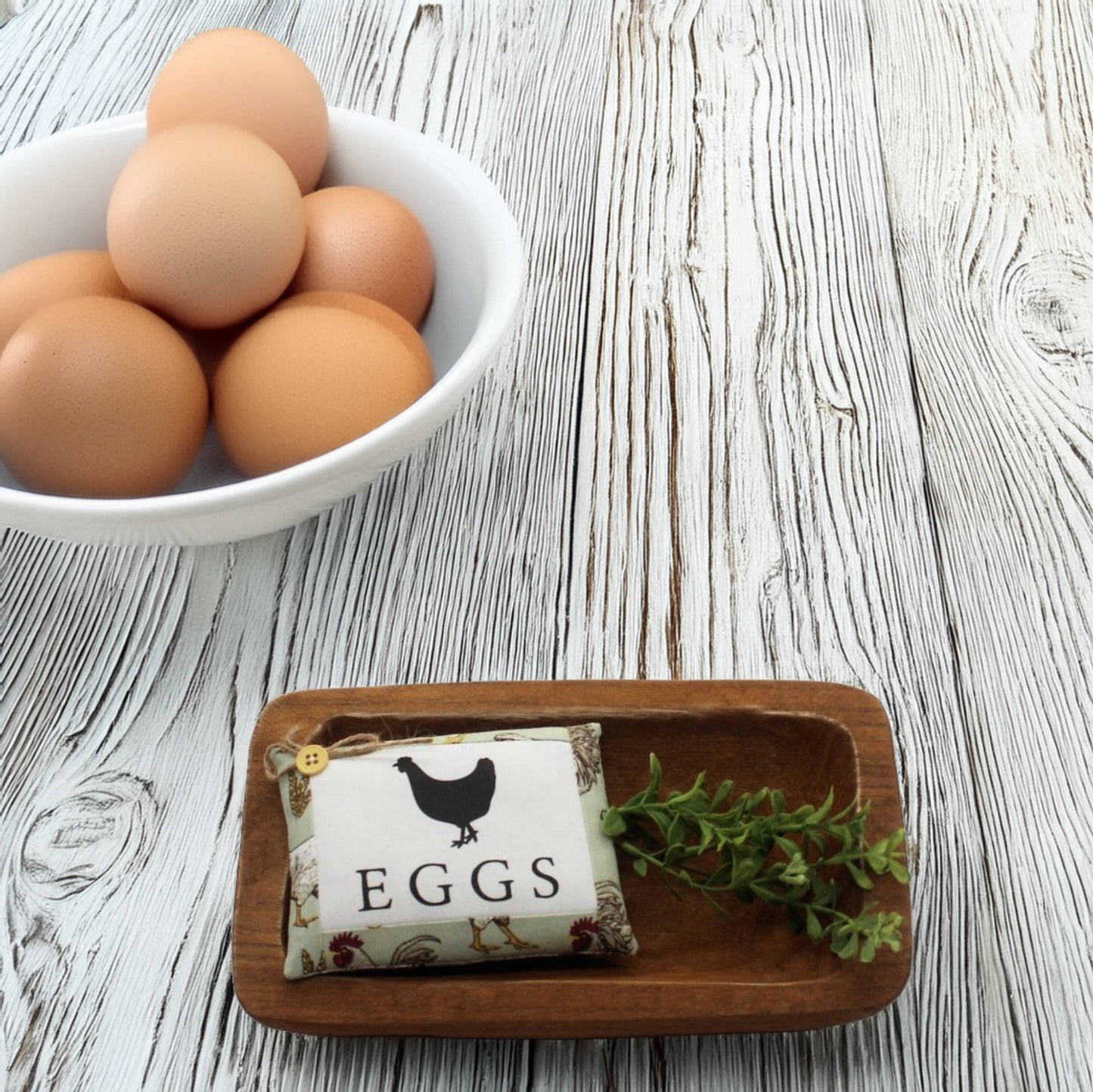 Bowl of eggs on a wooden surface with a decorative mini pillow sign labeled 'EGGS'.