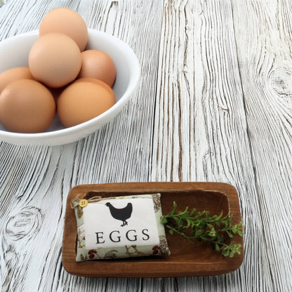 Bowl of eggs on a wooden surface with a decorative mini pillow sign labeled 'EGGS'.