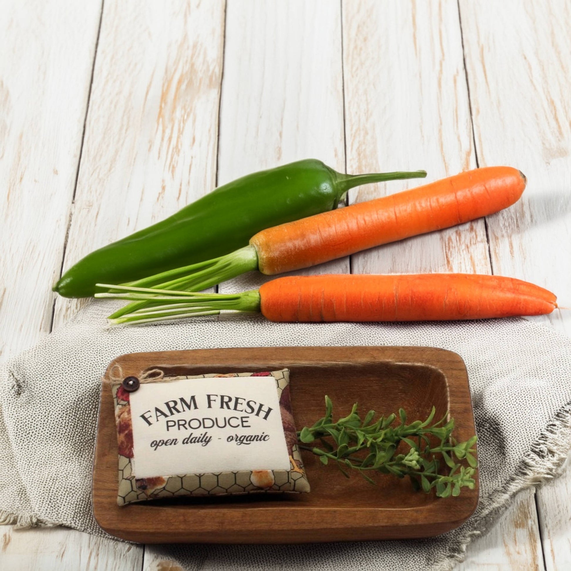Farm fresh produce including carrots, a green pepper, and a small sign on a wooden tray with a white background.