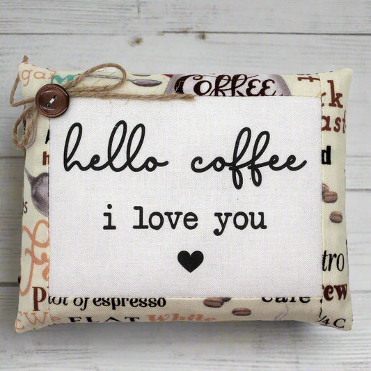 Decorative pillow tuck with 'hello coffee i love you' text on a wooden background