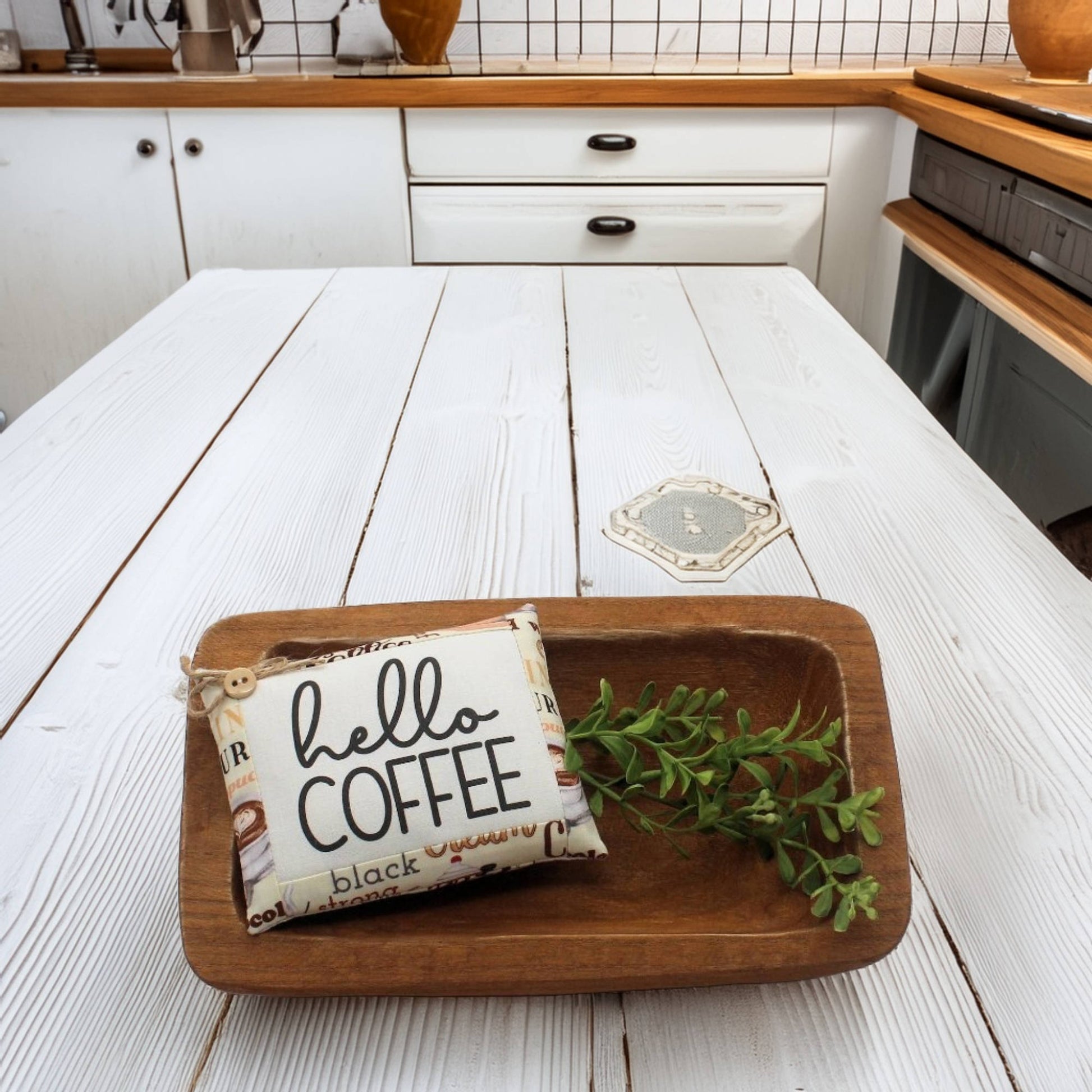 Wooden tray with a 'hello coffee' sign and a plant on a white wooden table.