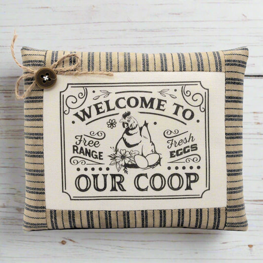 Decorative pillow with 'Welcome to Our Coop' text and chicken illustration on a wooden background