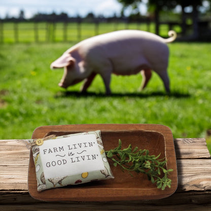 Mini pillow bowl filler sign with 'Farm Livin' is Good Livin' text on a wooden tray with a pig in the background
