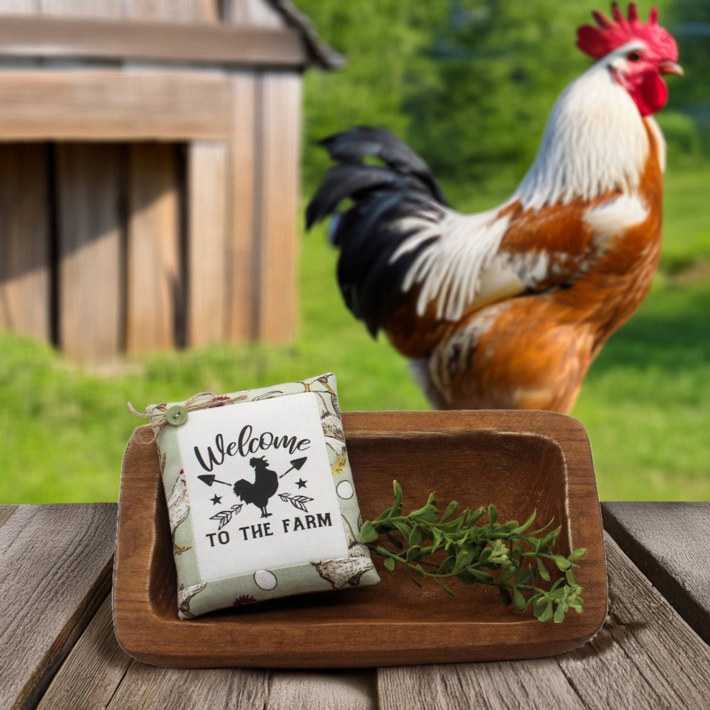 Decorative sign with rooster design on a wooden tray in front of a rooster in a farm setting.