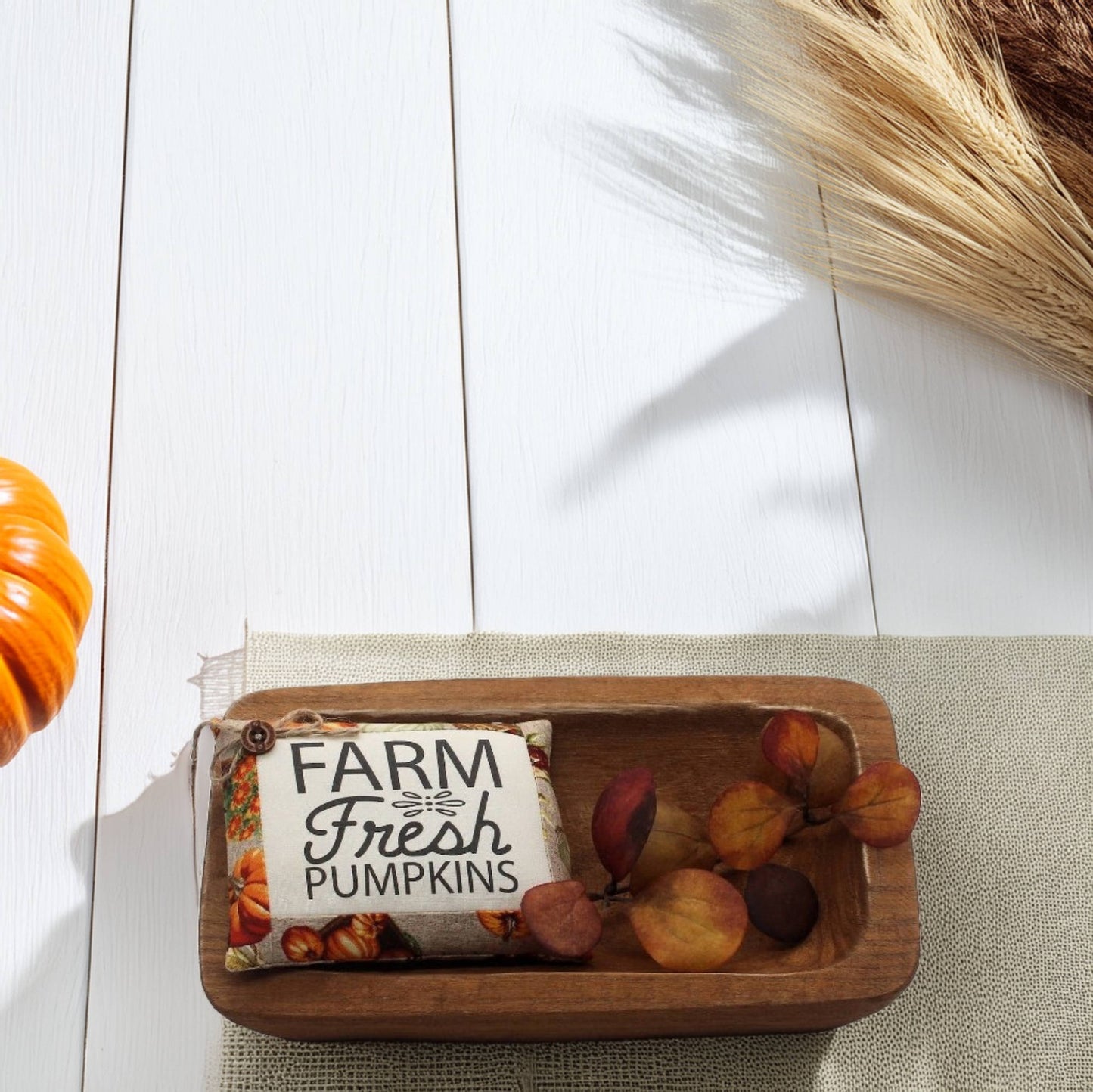 Wooden tray with a 'Farm Fresh Pumpkins' bowl filler sign on a white wooden surface.