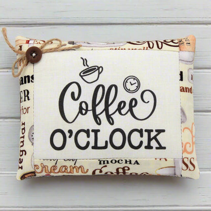 Fabric mini pillow with 'Coffee O'Clock' text and coffee-themed design on a wooden surface
