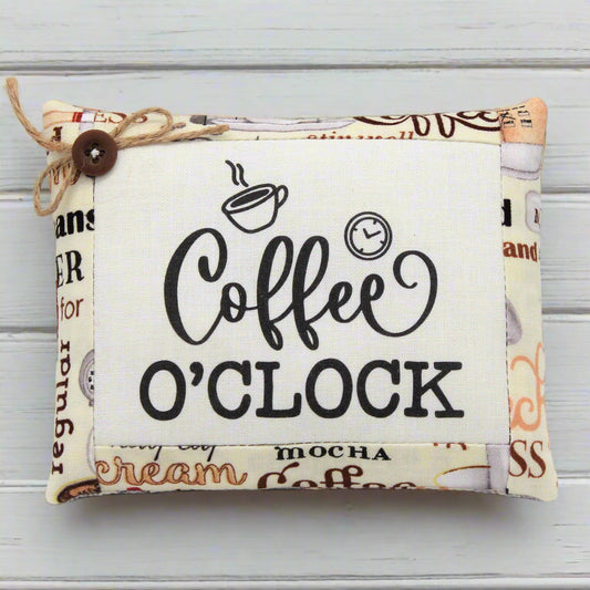 Fabric mini pillow with 'Coffee O'Clock' text and coffee-themed design on a wooden surface