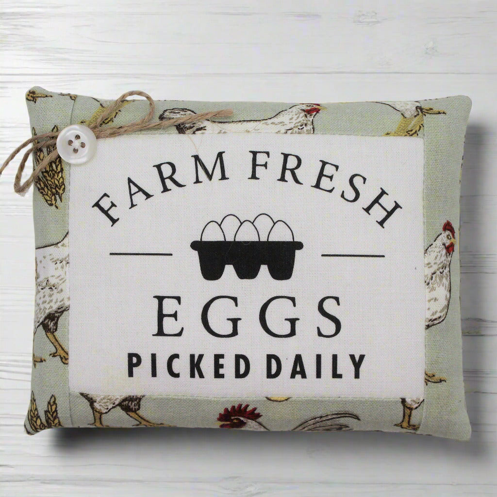 Decorative pillow tuck with 'Farm Fresh Eggs Picked Daily' text and chicken illustrations on a white wooden background.