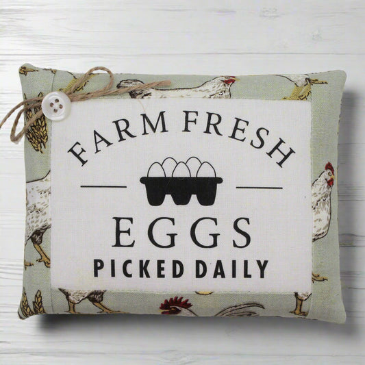 Decorative pillow tuck with 'Farm Fresh Eggs Picked Daily' text and chicken illustrations on a white wooden background.