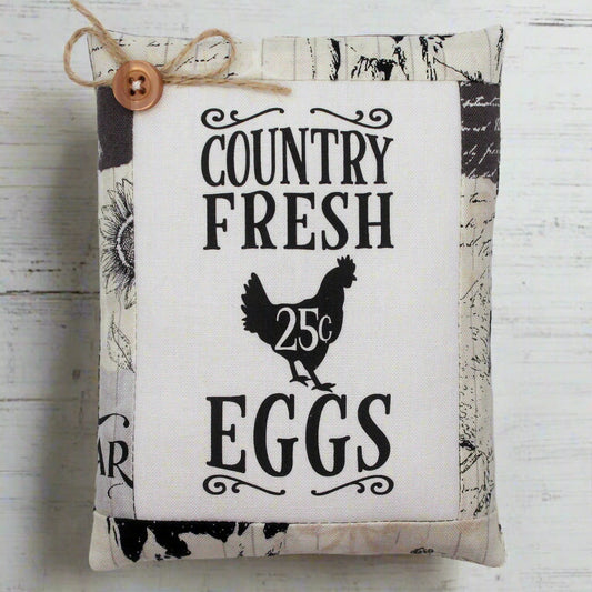 Fabric pillow tuck with 'Country Fresh Eggs' text and chicken illustration on a wooden background