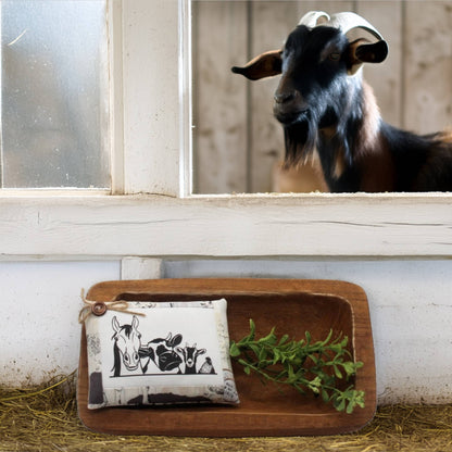 Goat looking at a wooden tray with a pillow tuck and leaves on a rustic background