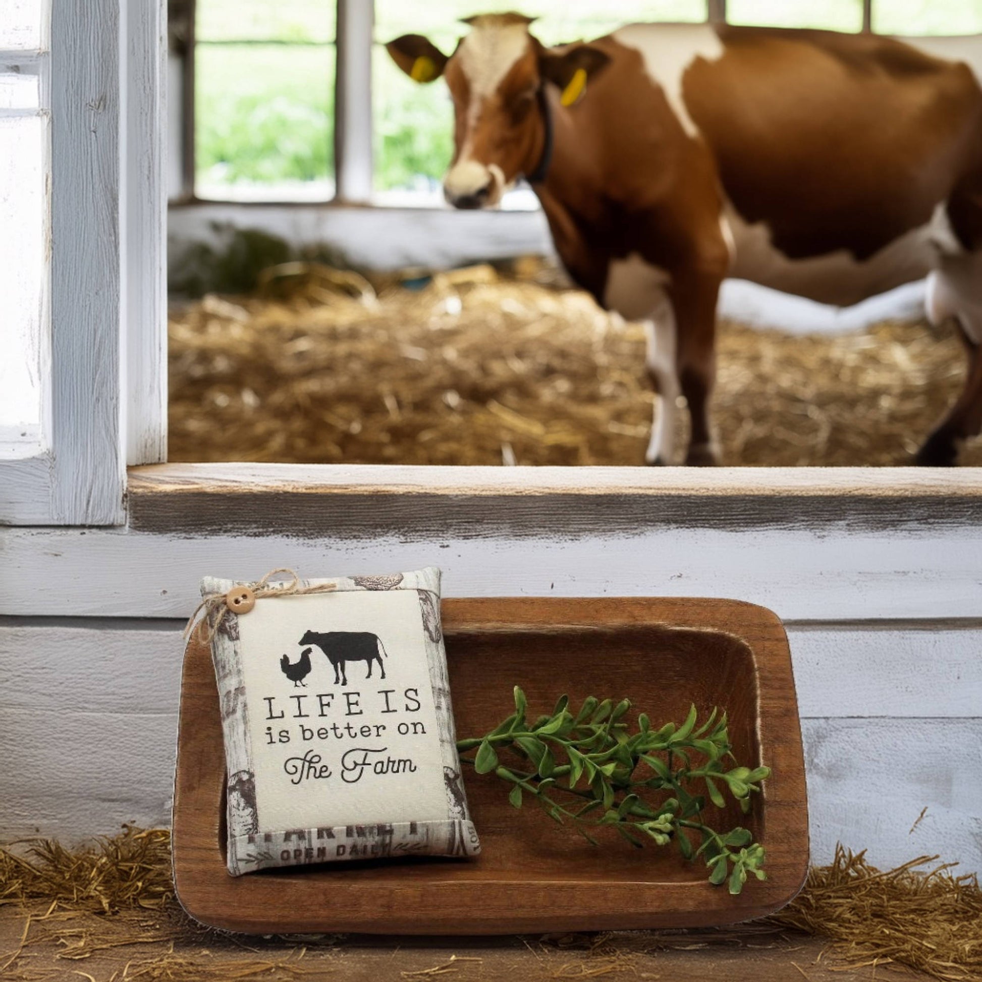Decorative sign with 'Life is better on the farm' text in a barn setting with a cow in the background.