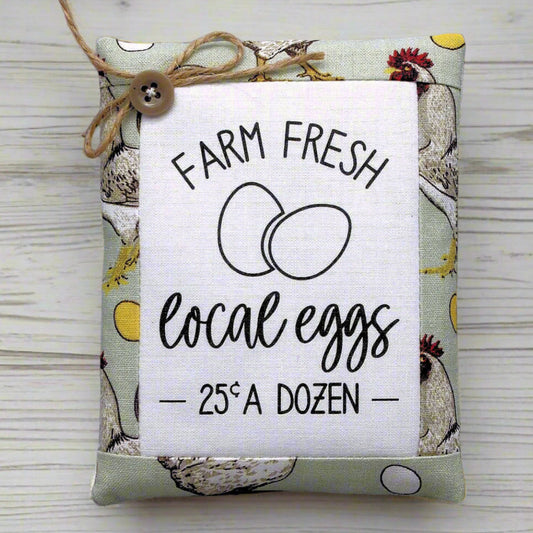Decorative miniature pillow with 'Farm Fresh Local Eggs' text on a wooden surface