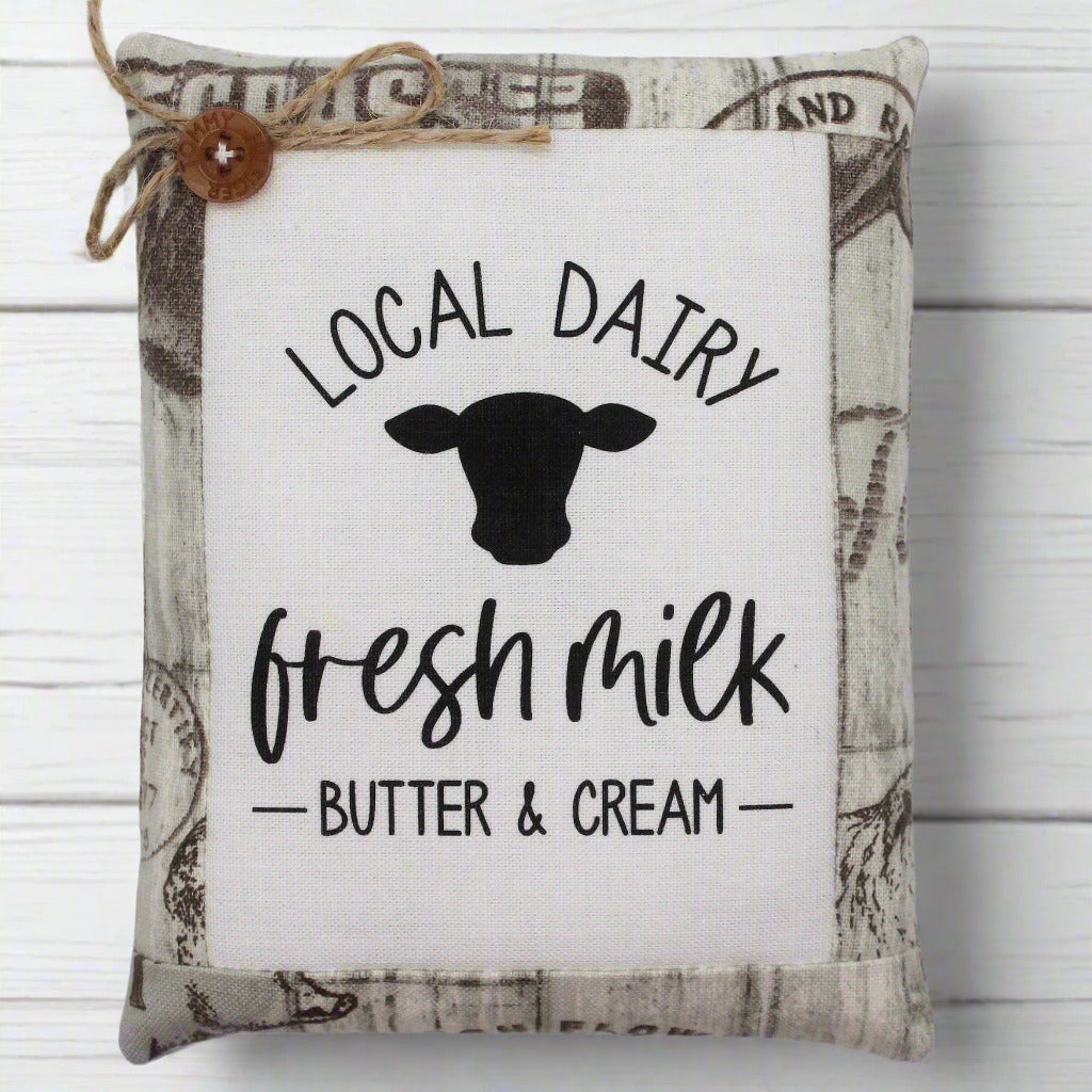 Decorative pillow tuck with 'Local Dairy, Fresh Milk, Butter & Cream' text and cow silhouette on a white background.