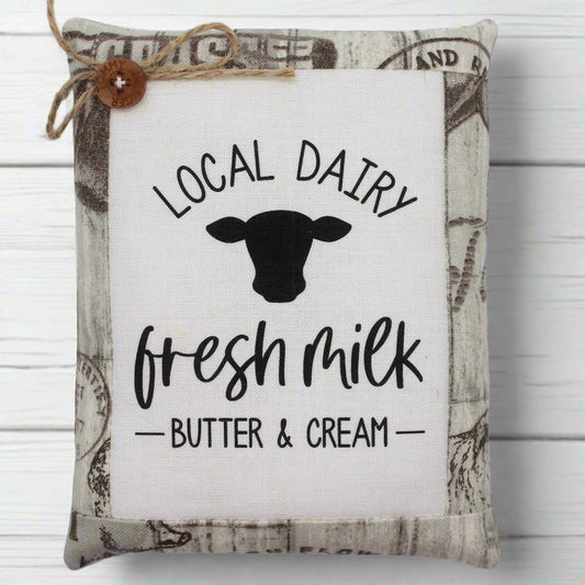 Decorative pillow tuck with 'Local Dairy, Fresh Milk, Butter & Cream' text and cow silhouette on a white background.