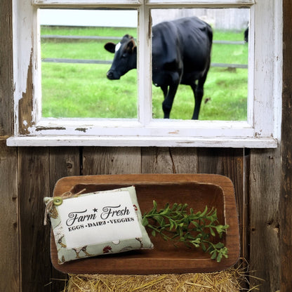 Wooden tray with a 'Farm Fresh' sign and greenery, cow visible through window in background