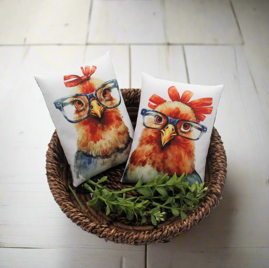 Two decorative pillows with chicken designs wearing glasses in a woven basket