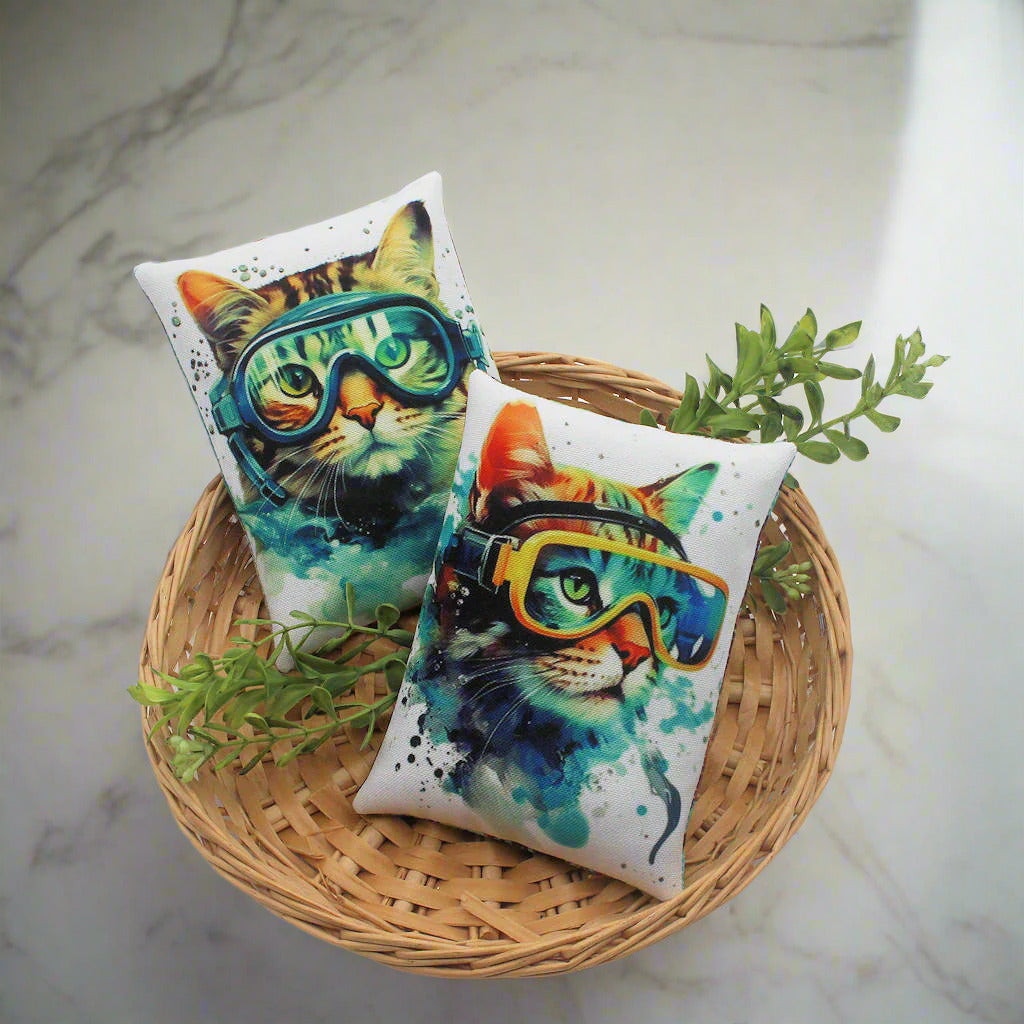 Two cat-themed pillows with goggles on a woven basket with greenery
