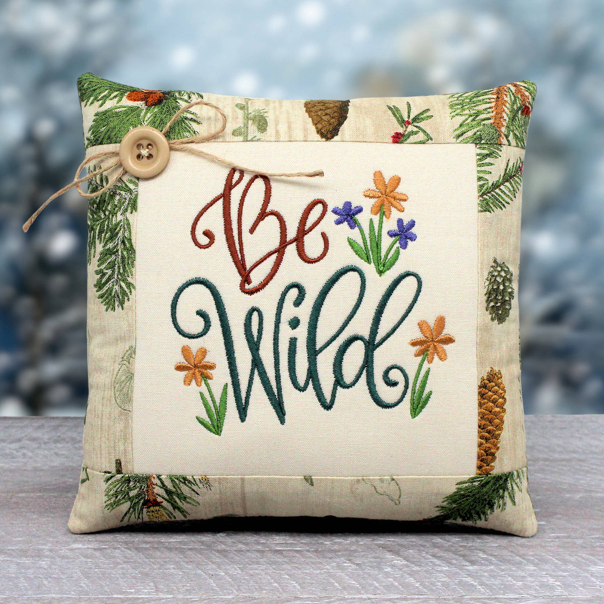 Small pillow tuck or bowl filler embroidered with 'be wild' alongside a cluster of wildflowers.