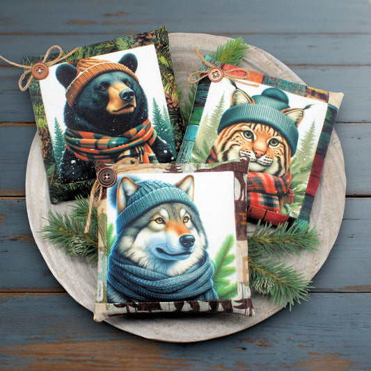 Three decorative mini pillows with animal illustrations wearing hats and scarves on a wooden surface.