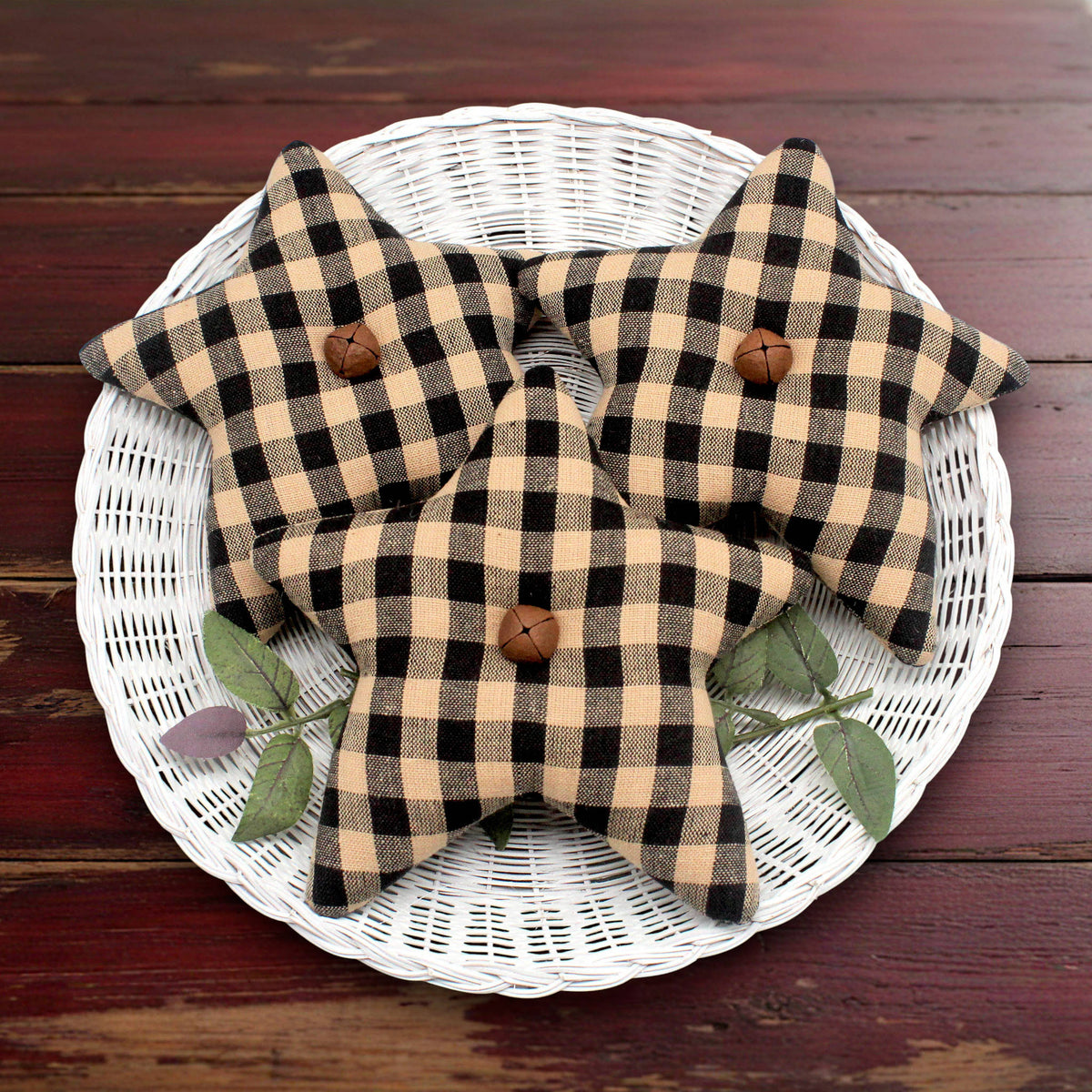 Three fabric stars bowl fillers in a black and tan buffalo plaid pattern, arranged on a white wicker tray over a dark wooden surface.