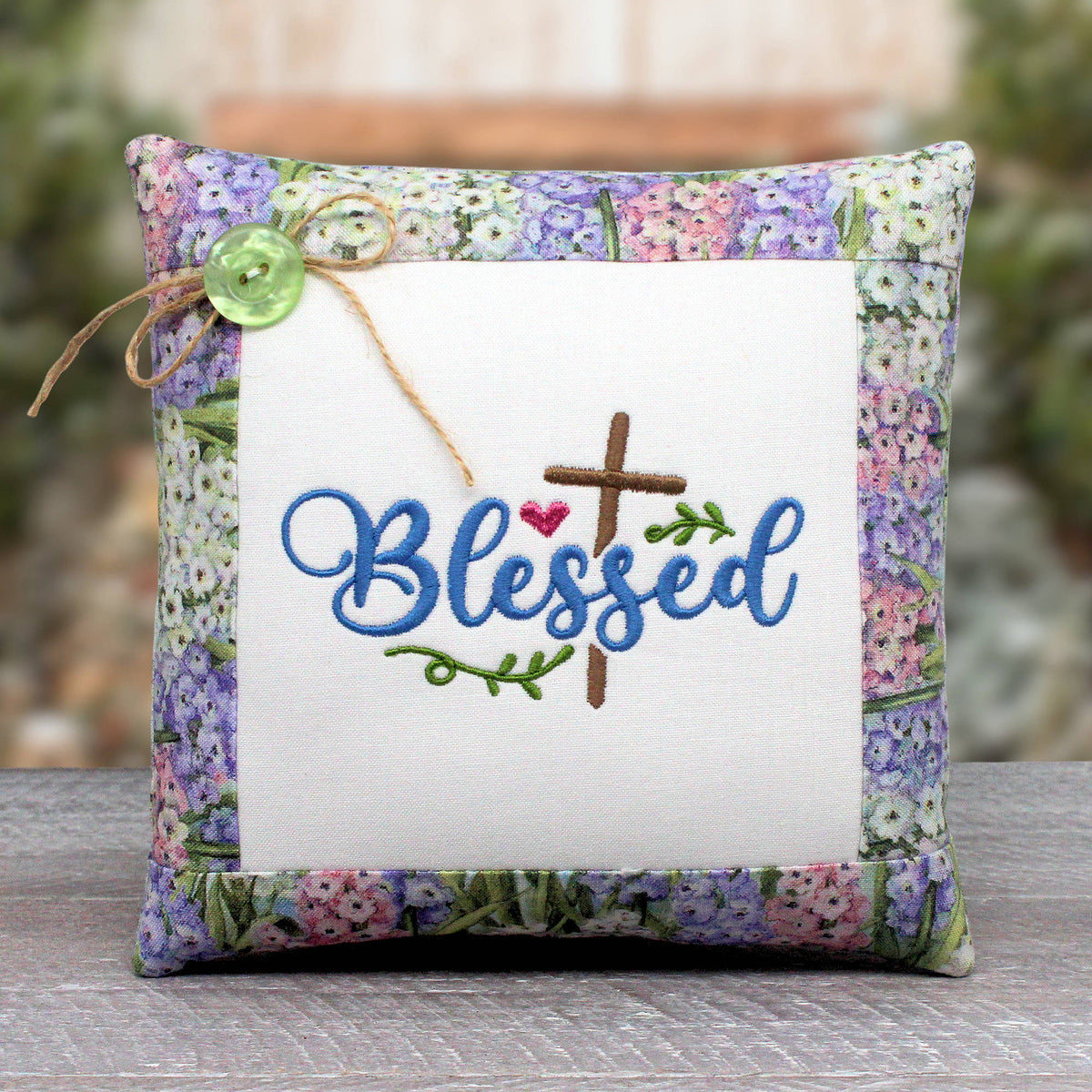 Small pillow tuck or bowl filler embroidered with the word 'blessed' alongside a Christian cross, trimmed with a fabric with a pastel floral print