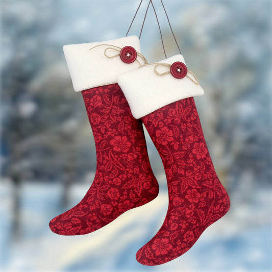 Two burgundy Christmas stockings with a floral pattern and white fleece cuffs, hanging against a blurred snowy outdoor background.
