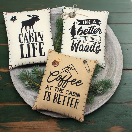 Three decorative pillows with cabin-themed text on a wooden surface.