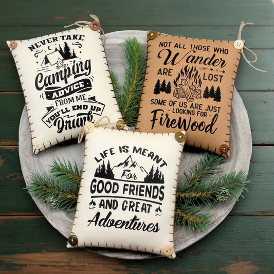 Three motivational quotes on fabric with camping theme on a wooden surface.