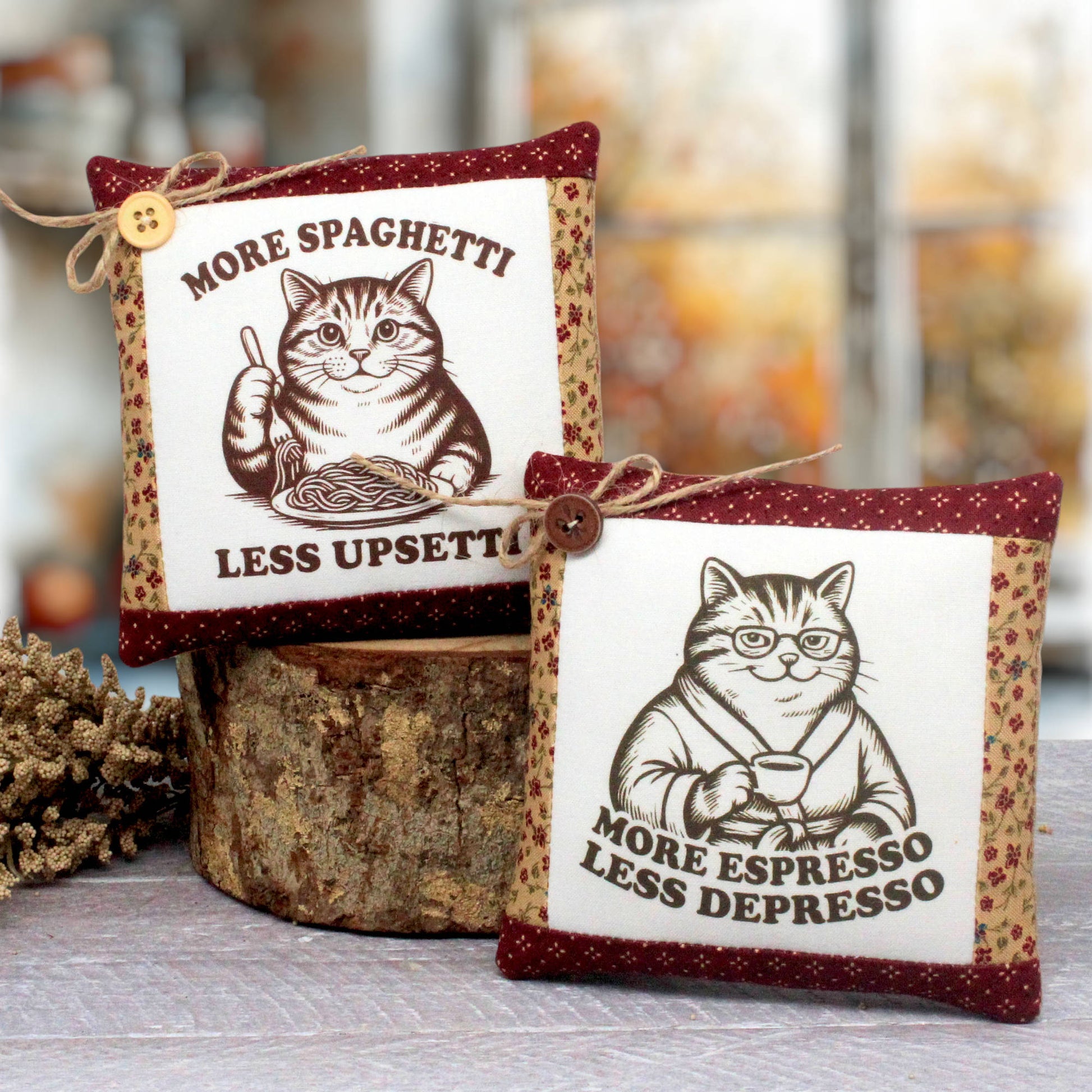 Two decorative fabric mini pillows with cat illustrations and food-themed phrases, displayed on a rustic wood slice with a blurred indoor background.