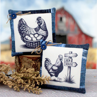 Two small decorative mini pillows with a rustic farm theme, featuring dark blue and white illustrations of a hen and rooster on a white background with blue denim-style borders. One pillow cover shows a hen with eggs in a basket, and the other shows a rooster next to a sign that reads 'HEN HOUSE'.