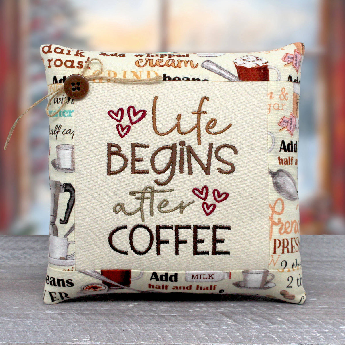 Small pillow tuck or bowl filler embroidered with the phrase 'life begins after coffee.' The center panel is trimmed with a cotton print fabric with a coffee-themed design.