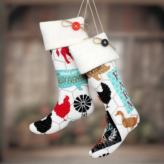 Two white Christmas stockings with a colorful farm-themed print, hanging against a blurred rustic background. One stocking features red chickens and a windmill