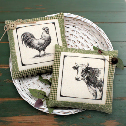 Set of two fabric mini pillow bowl fillers featuring vintage-style images of a cow and a rooster, displaying in a white basket against a green wooden table