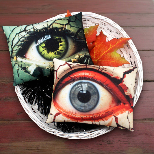 Two eye-themed pillows with vibrant colors on a woven basket with autumn leaves.