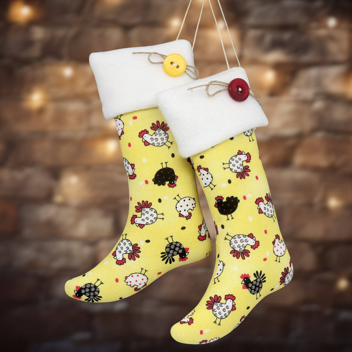 Two yellow Christmas stockings with a chicken print, white fleece cuffs, and decorative buttons, hanging against a blurred rustic brick wall with warm lights.