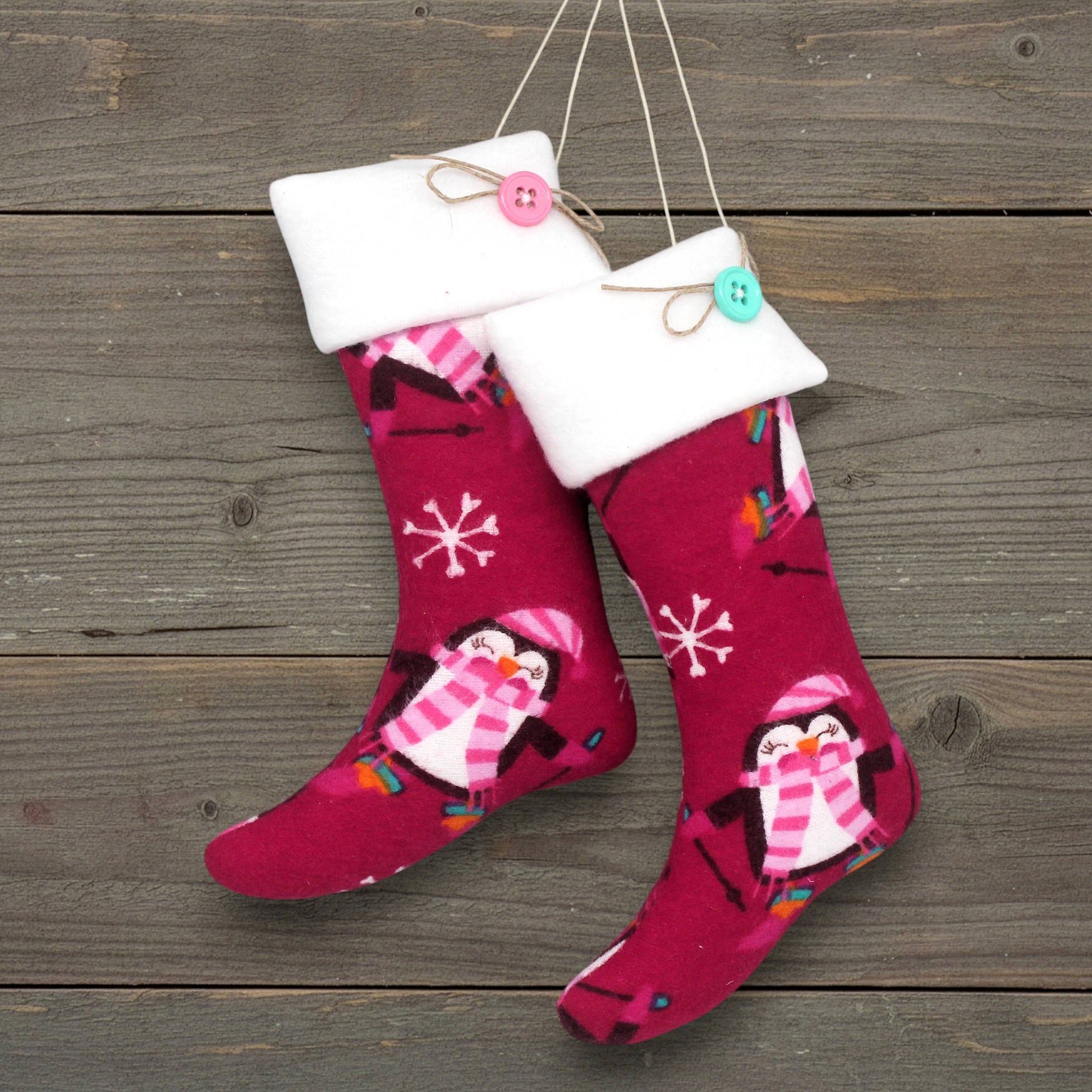 Pair of handmade Christmas stocking ornaments with penguins on a deep pink background