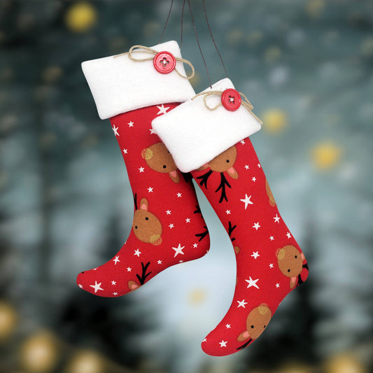 Two red Christmas stockings with white fleece trim, hanging from thin strings. The stockings are decorated with brown reindeer faces, black antlers, and white stars, and each has a small red button with tan ribbon at the top.
