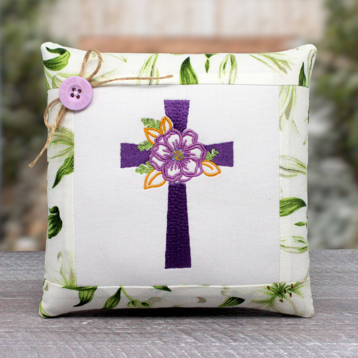 Small pillow tuck or bowl filler features a center panel machine-embroidered with a Christian cross with a floral design.  It's trimmed with a cotton print fabric with white lilies.