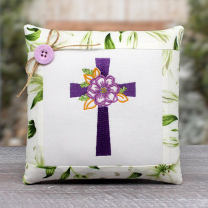 Small pillow tuck or bowl filler features a center panel machine-embroidered with a Christian cross with a floral design.  It's trimmed with a cotton print fabric with white lilies.