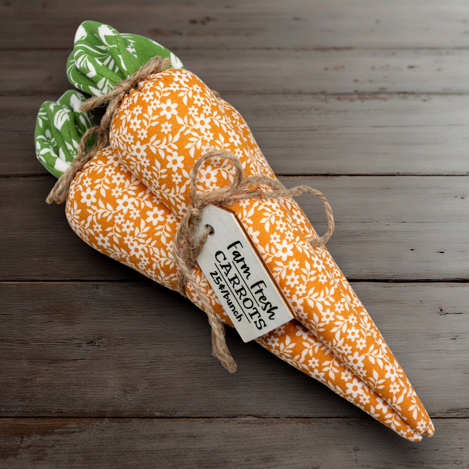 Decorative fabric carrots with a tag on a wooden surface