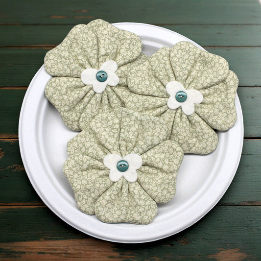 Fabric flowers with green and white colors on a white plate against a wooden background