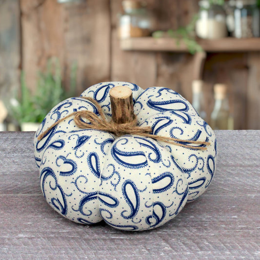 A fabric decorative pumpkin with a blue paisley pattern on a cream background, tied with natural twine and a small wooden stem, displayed on a rustic wooden surface.