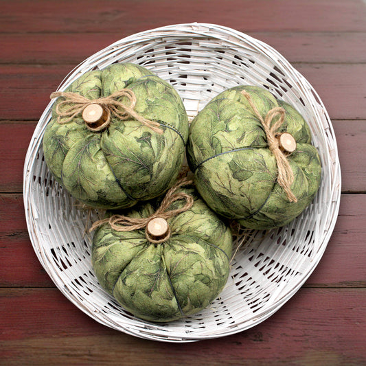 Three green decorative pumpkins with twine on a white woven basket against a wooden background