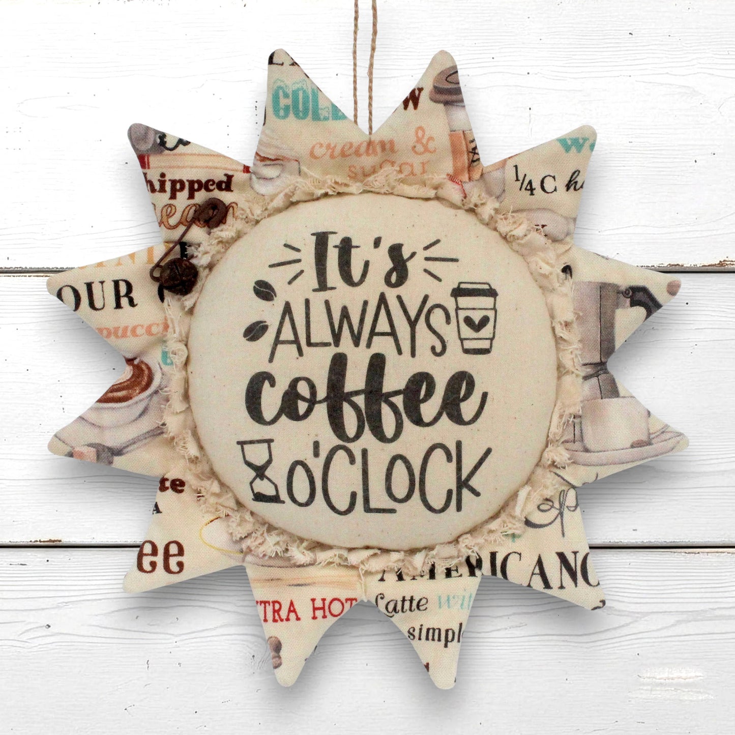 A sunflower-shaped decorative wall hanging with a central round disc that reads “It’s ALWAYS coffee o'clock,” surrounded by pointed rays made from vintage-style coffee-themed paper with a ruffled fabric trim.