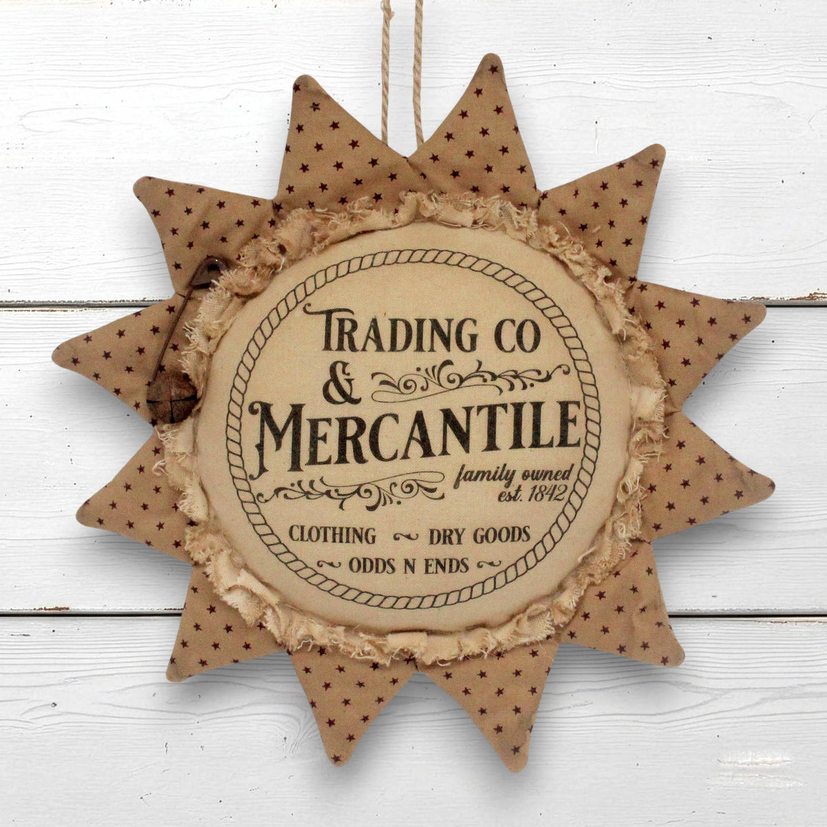 A rustic sunflower-shaped hanging ornament with a central round plaque reading 'Trading Co & Mercantile' and decorative text around it, shown against a white painted wood background.