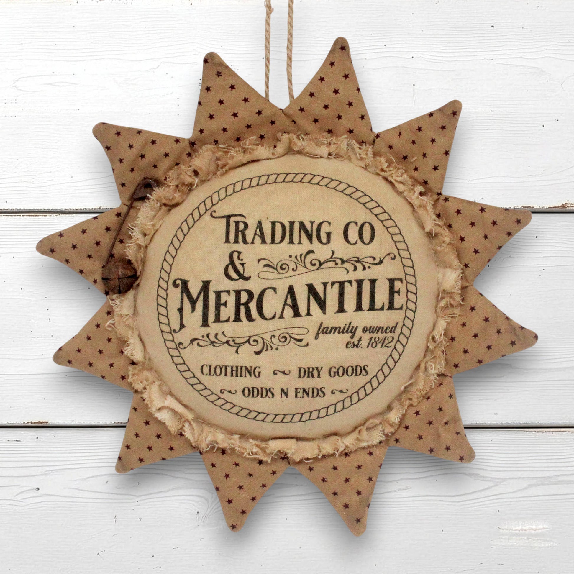 A rustic sunflower-shaped hanging ornament with a central round plaque reading 'Trading Co & Mercantile' and decorative text around it, shown against a white painted wood background.