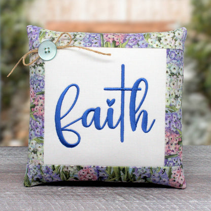 Small pillow tuck or bowl filler machine embroidered with the word 'faith.' A cross represents the t in the word.  It's trimmed with a pastel floral print fabric.